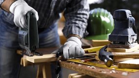 Adult carpenter craftsman wears protective leather gloves, with electric saw working on cutting a wooden table. Construction industry, housework do it yourself. Footage.