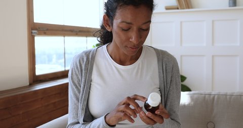 Young african woman read drug medicine prescription label, ill sick mixed race lady holding bottle taking medicine pills tablets worried about side effects, close up view, pharmacy healthcare concept