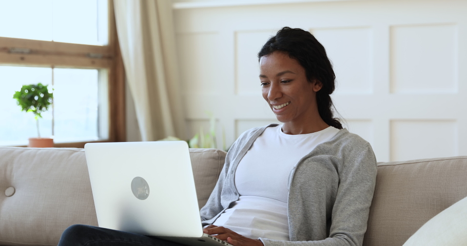 Smiling mixed race lady sit on couch using laptop notebook at home, happy young african american woman typing on computer browsing surfing internet look at screen having fun chatting in social media | Shutterstock HD Video #1039317665