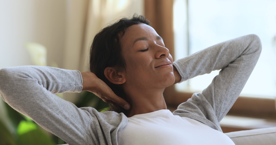 Relaxed happy healthy young african woman resting in cozy home enjoying stress free weekend looking dreaming breathing fresh air lounge on comfortable sofa hands behind head, peace of mind concept | Shutterstock HD Video #1039317692