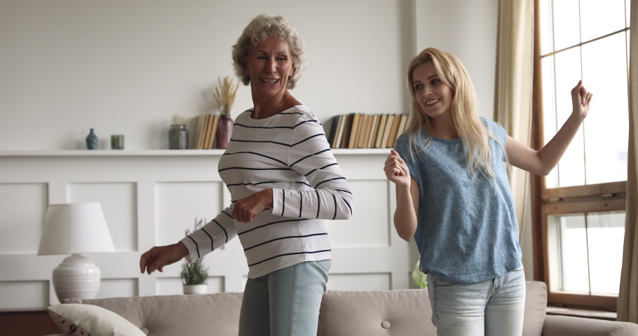 Happy carefree two age generation women family young grown adult daughter and healthy active old senior mature mother listening music dancing together laughing having fun at home in living room Royalty-Free Stock Footage #1039317716