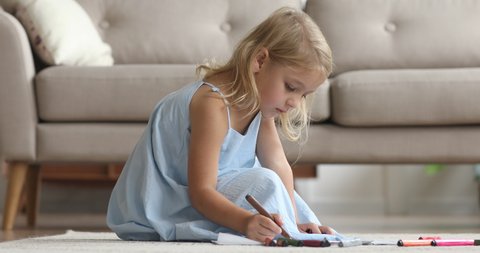 Cute small kid girl artist playing alone drawing coloring picture with felt pen sit on floor, focused smart preschool child enjoying creative art hobby activity at home, children development concept