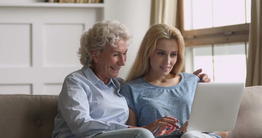 Happy two age generation women family senior mother and adult daughter have fun enjoy using laptop at home sit on sofa, old mom embrace young woman bonding shopping online looking at computer screen | Shutterstock HD Video #1039317773