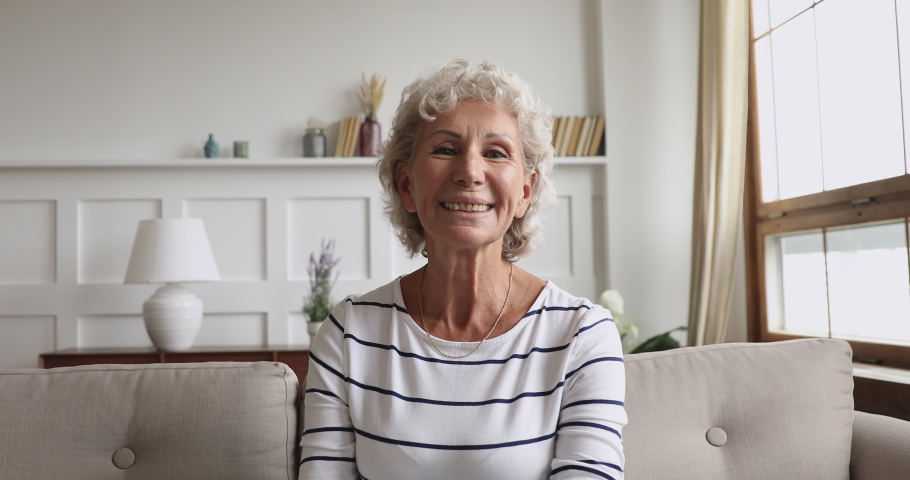 Happy senior old grandmother talking to camera at home, smiling middle aged elderly woman sit on sofa communicating by webcam in distance conference video call chatting laughing looking at webcamera Royalty-Free Stock Footage #1039317803