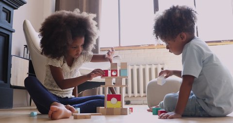 Two cute little african children siblings play with wooden blocks on warm heated floor at home kindergarten, small mixed race kids boy and girl building castle of toys, children development concept