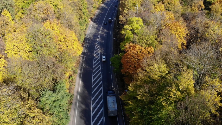 Cars go on the road. Highway through the forest. Logistics and transportation. Drive a car through the autumn forest. Logistics and transportation.