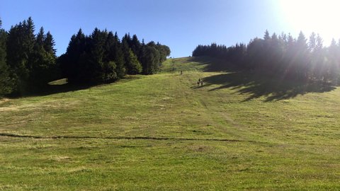 Group of people hiking. Biker rides a bike down the hill in ski resort. Tourist silhouettes walking. Ski area in Sachticky, Slovakia in summer. 