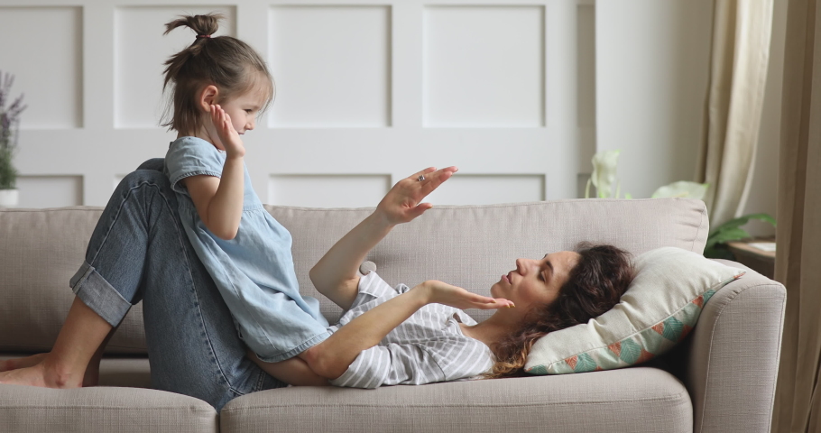 Happy parent mom and cute kid daughter playing patty cake at home, carefree family of young mother and little child girl clap hands having fun together laughing enjoying funny game relaxing on couch Royalty-Free Stock Footage #1039337843