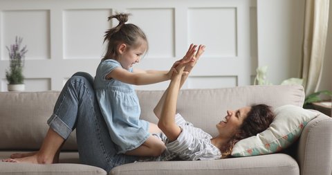 Happy parent mom and cute kid daughter playing patty cake at home, carefree family of young mother and little child girl clap hands having fun together laughing enjoying funny game relaxing on couch