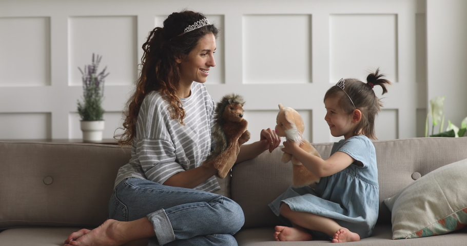 Happy family young mom babysitter or nanny wearing crown holding toys having fun with cute small child daughter sit on sofa, mother queen and little kid girl bonding playing puppets together at home Royalty-Free Stock Footage #1039337855
