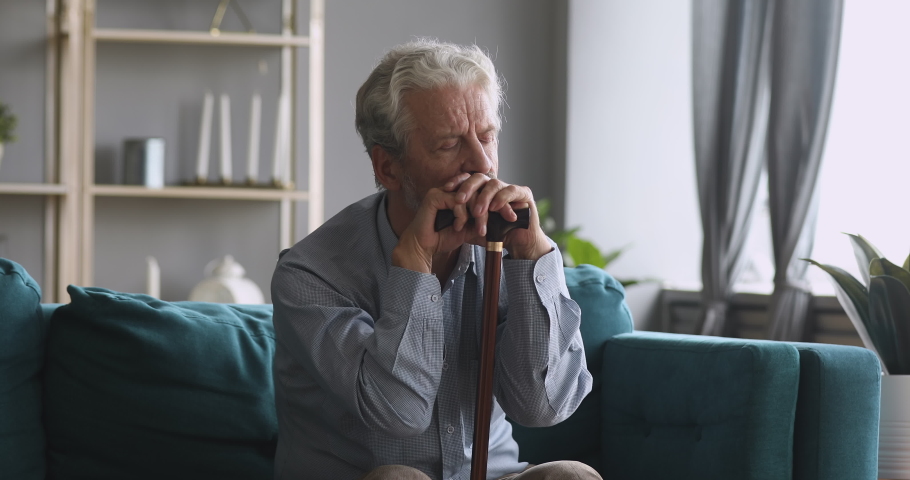 Thoughtful sad lonely old elder grandfather hold cane stick sit alone on couch, upset depressed senior retired man having geriatric health problem think of loneliness disease in retirement house | Shutterstock HD Video #1039337858