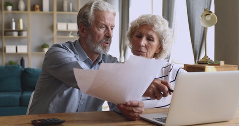 Worried senior retired couple checking calculating bills bank loan payment doing paperwork discuss unpaid debt taxes, stressed old grandparents family look at laptop upset about money problem concept