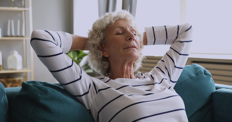 Healthy serene senior woman rest on comfortable sofa with eyes closed breathing fresh air hold hands behind head, calm relaxed old grandmother enjoy doing breathe exercises feel peace of mind at home | Shutterstock HD Video #1039337918