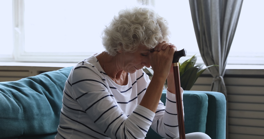 Senior lonely sad woman sitting alone at home holding walking cane stick in hands suffer from injury, grief, bones disease or depression, worried hopeless older disabled people health care concept | Shutterstock HD Video #1039337921