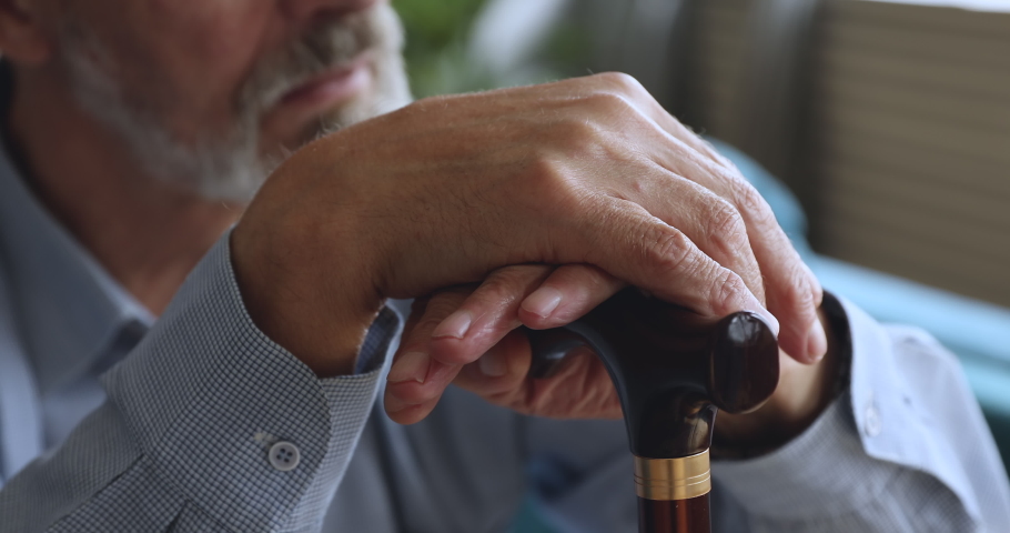 Elderly senior adult man holding walking cane stick in hands concept, sad depressed lonely old retired disabled male grandparent sit alone at home waiting medical care support concept, close up view | Shutterstock HD Video #1039337939