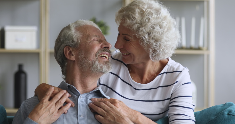 Happy loving elderly old couple grandma and grandpa embracing bonding relaxing sit on couch looking at camera, smiling senior retired family enjoy hugging on sofa in living room grandparents portrait Royalty-Free Stock Footage #1039337957