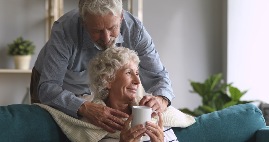 Loving senior husband grandfather cover old mature grandmother sit on sofa drink tea with blanket plaid showing care warming embracing elderly wife enjoy autumn leisure retirement lifestyle at home | Shutterstock HD Video #1039337975