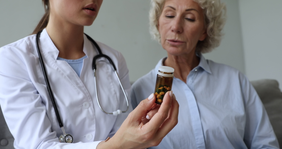 Female doctor pharmacist holding medicine pills bottle explaining prescription to older woman patient prescribing drug at medical consultation, seniors healthcare and pharmacy concept, close up view Royalty-Free Stock Footage #1039338038