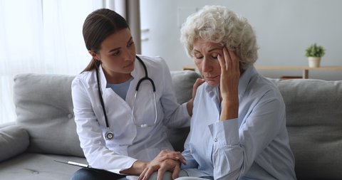 Young woman caregiver nurse doctor supporting comforting consoling sad depressed old grandma patient having serious disease giving empathy and help concept at medical consultation in hospital home.