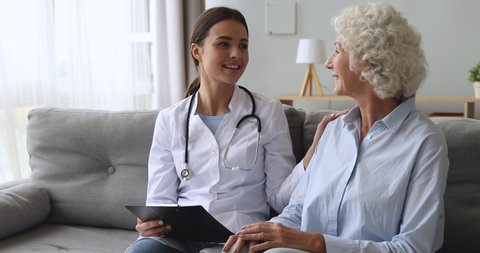 Caring young female nurse caretaker doctor helping talking with senior grandmother patient give support empathy encouraging elderly woman at medical visit, older people healthcare recovery concept