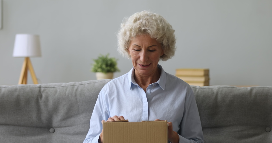 Happy old senior woman customer hold open parcel box sit on sofa in living room, smiling elderly grandma customer receive post shipment online shop sale order satisfied with fast delivery concept Royalty-Free Stock Footage #1039338092