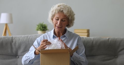 Happy old senior woman customer hold open parcel box sit on sofa in living room, smiling elderly grandma customer receive post shipment online shop sale order satisfied with fast delivery concept