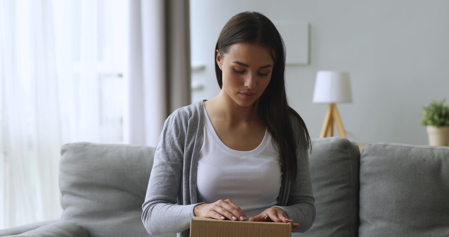 Satisfied female customer open online order shopping courier delivery parcel sit on sofa, happy young woman holding cardboard box unpack receive good purchase by post mail shipping at home concept | Shutterstock HD Video #1039338107