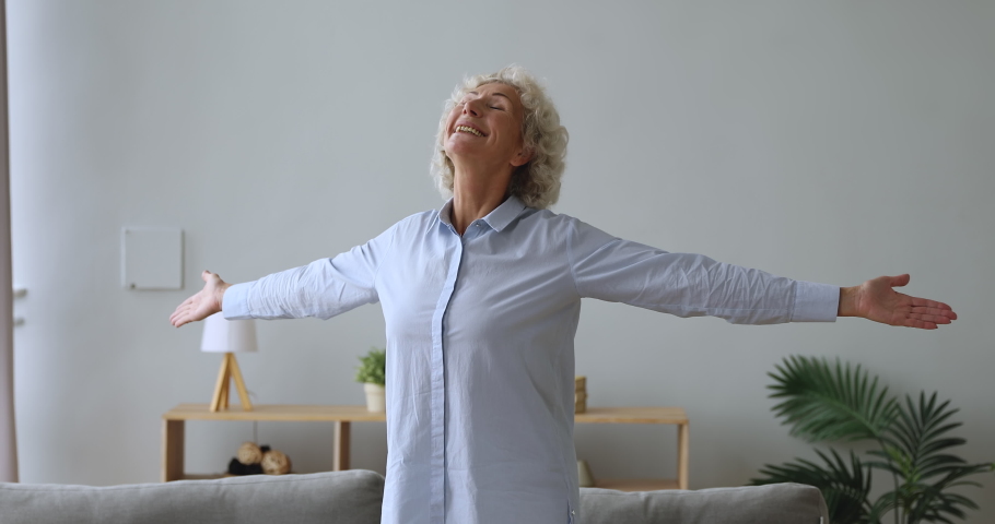 Overjoyed happy senior woman stand in modern living room interior alone with arms outstretched enjoy wellbeing in cozy new home, excited old grandma feel motivated in furnished renovated flat concept | Shutterstock HD Video #1039338119