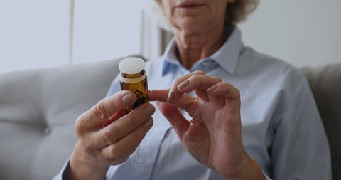 Old senior woman grandma read drug prescription label pour two pills from medication bottle hold painkiller capsules on hand take medicine, elderly people healthcare, pharmacy concept, close up view