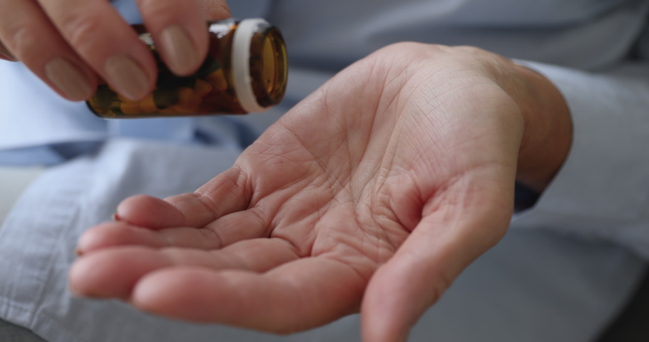 Senior adult woman holding painkiller pills on female hand pouring two capsules from meds bottle taking medicine, old elderly grandmother health care, pharmacy and treatment concept, close up view | Shutterstock HD Video #1039338155