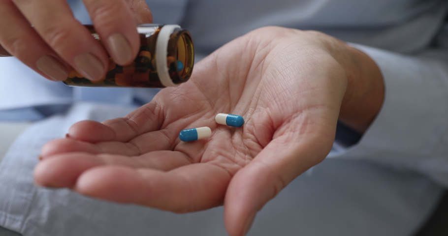 Senior adult woman holding painkiller pills on female hand pouring two capsules from meds bottle taking medicine, old elderly grandmother health care, pharmacy and treatment concept, close up view | Shutterstock HD Video #1039338155
