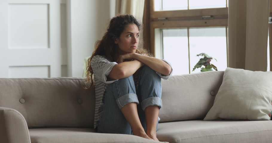 Thoughtful sad worried young woman sit alone on couch embracing knees troubled with loneliness, depressed lady feel upset jealous regret mistake abortion, having psychological mental problem concept Royalty-Free Stock Footage #1039338227