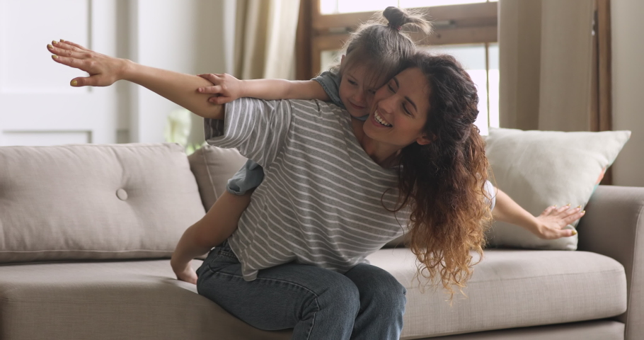 Happy family loving young mum playing piggybacking cute little funny kid daughter sit on couch at home, cheerful mother carrying small child girl on back bonding pretending flying having fun together Royalty-Free Stock Footage #1039338245