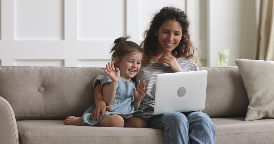 Happy parent mother and cute small child daughter looking at laptop screen webcam having fun using funny face mask effects making conference video call chat at home relaxing laughing sitting on sofa