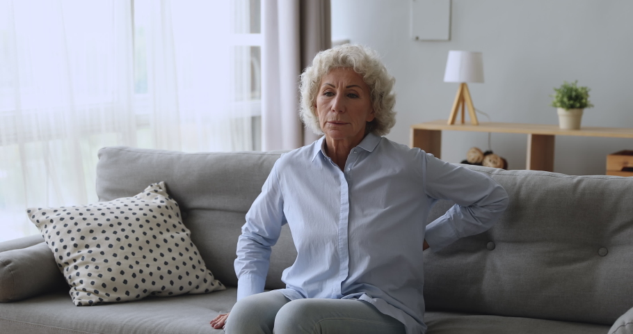 Upset worried senior adult woman feel sore back ache getting up from sofa, tired elderly grandma touching spine suffer from osteoarthritis lower lumbago spinal backache, older people backpain concept Royalty-Free Stock Footage #1039338344