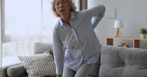 Upset worried senior adult woman feel sore back ache getting up from sofa, tired elderly grandma touching spine suffer from osteoarthritis lower lumbago spinal backache, older people backpain concept