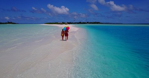 romantic couple taking a walk on the sandbar, Maldives while holding hands and colorful umbrella, Love and relationship concept, Extreme long drone shot, background with copy space
