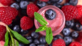 Top view of fresh blended fruit smoothierotating among forest berries, 4K video shot 2in1. Protein ingredients for human health. Fresh colorful forest berries and full vitamin complex