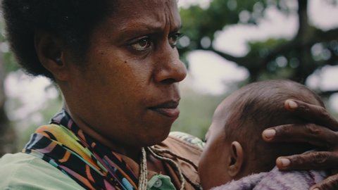 Melsisi, Pentecost Island / Vanuatu - MAY 10 2019: traditional black melanesia woman mother with her cute kid child at the edge of the topical rainforest jungle closeup