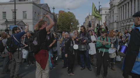 London , London / United Kingdom (UK) - 10 09 2019: A senior citizen at an Extinction Rebellion demonstration with demonstrators playing on drums on Whitehall road in Westminster.