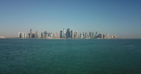 Aerial rising day view of Doha corniche and business district in Qatar, with skyscrapers and urban skyline in the background on the waterfront of the persian gulf, west bay area