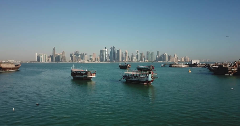 Aerial flying forward view of Doha boat harbour with skyscrapers and West Bay business district in the background, futuristic capital city of Qatar, corniche on the waterfront