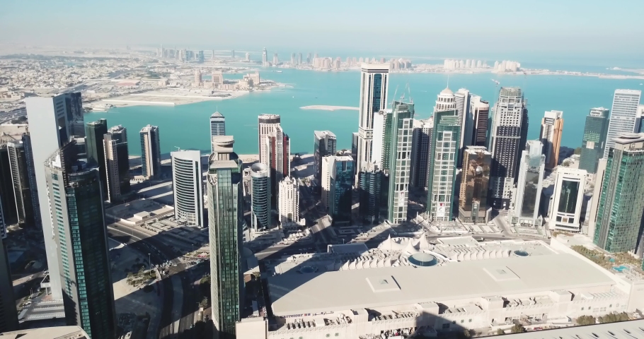 Aerial moving-forward view of futuristic global city in the desert, with high buildings and towers, near the sea, Doha, Qatar