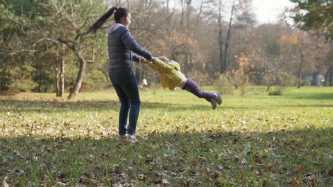 Baby girl with her mother have fun in the autumn park. Slow motion of mother and baby girl spinning around. Happy family concept.