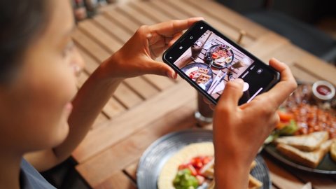 Young Woman Taking Photo of Healthy Breakfast Using Mobile Phone in Vegan Restaurant. 4K Slowmotion Flatlay Food Photography on Wooden Table in American Diner. Thailand. Video Stok