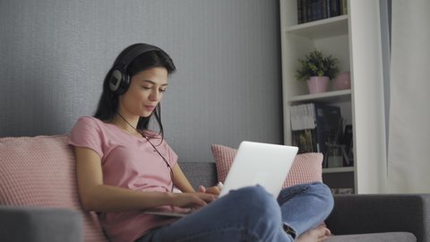 Young Beautiful Brunette with headphones Works on a Laptop Computer at home
