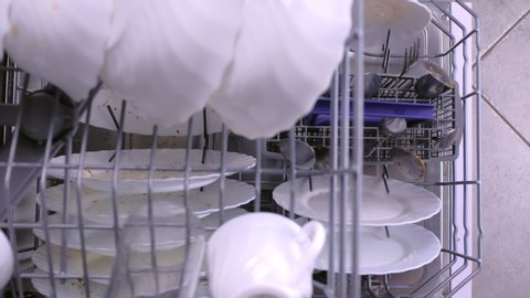 Man is putting a cups in dishwasher and pushing baskets in dishwasher. Top view, close-up hand.