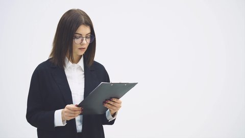 Lovely businesswoman in suit standing with clipboard in her hands, looking at it with misunderstanding on her face, showing it to the camera. The question mark is written.