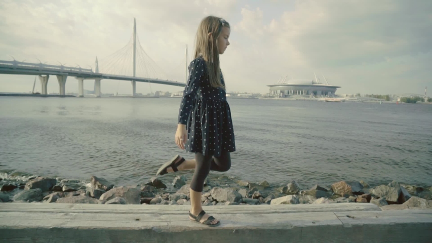 Slender girl bending back and keeping her foot behind on a seacoast in slo-mo