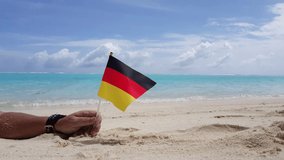 man hand holding german flag in his hand lying down on the white sand of the tropical beach - Powered by Shutterstock - Get 15% off with code: PIKWIZARD15